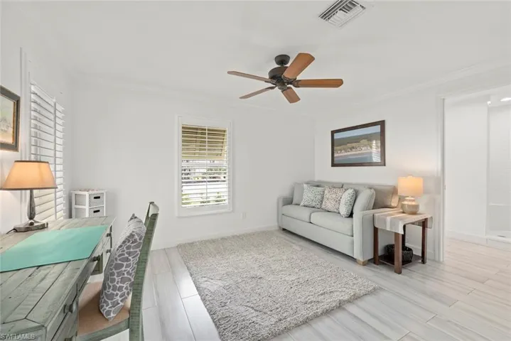 Living room with baseboards, visible vents, a ceiling fan, ornamental molding, and wood finished floors