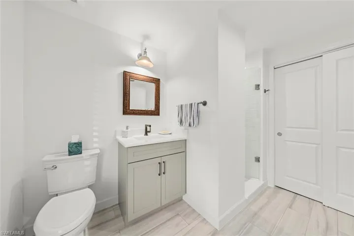 Full bathroom with toilet, vanity, baseboards, a shower stall, and wood tiled floor