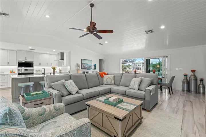 Living room featuring lofted ceiling, recessed lighting, visible vents, light wood-style floors, and ornamental molding