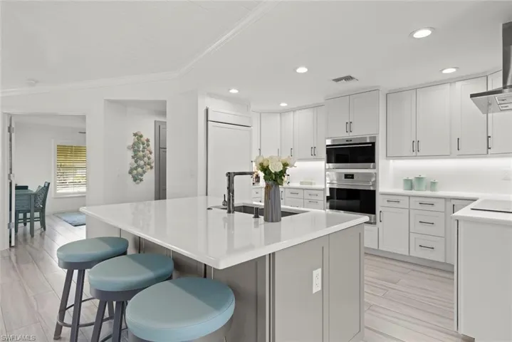 Kitchen with a breakfast bar, visible vents, stainless steel double oven, a sink, and paneled refrigerator