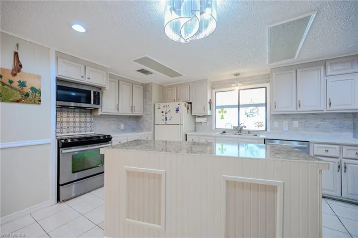 Kitchen with appliances with stainless steel finishes, a sink, light tile patterned floors, a textured ceiling, and a kitchen island