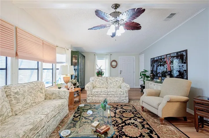 Living area with a textured ceiling, wood finished floors, ceiling fan, crown molding, and lofted ceiling