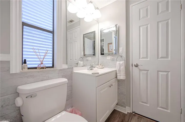 Bathroom featuring toilet, vanity, tile walls, ornamental molding, and a chandelier with tub/shower