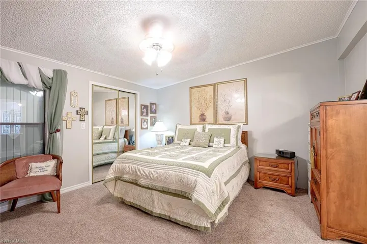 Bedroom with light colored carpet, crown molding, a textured ceiling, a closet, and ceiling fan