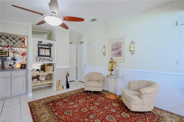 Sitting room featuring wainscoting, a textured ceiling, ceiling fan, light tile patterned flooring, and crown molding
