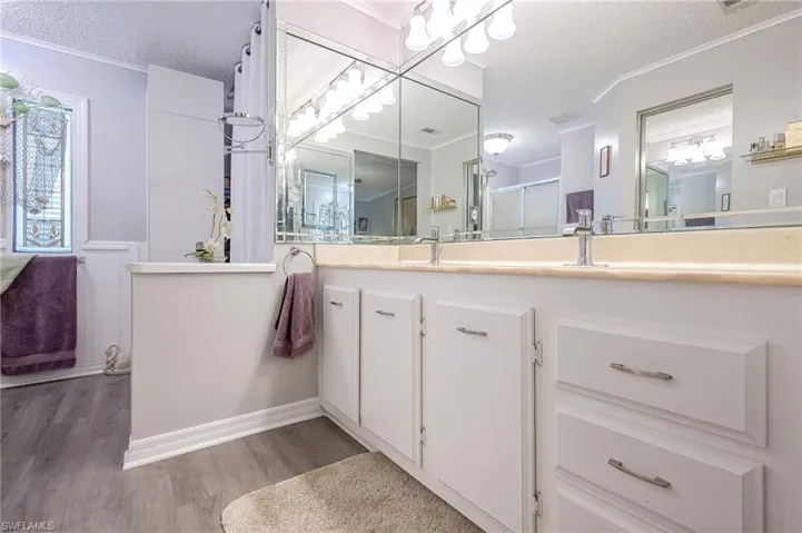 Full bathroom with a textured ceiling, wood finished floors, vanity, crown molding, and a shower with door