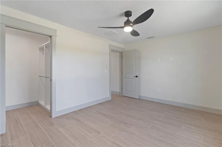 Second bedroom featuring ceiling fan, a textured ceiling, wood tile floors, and a custom walk in closet
