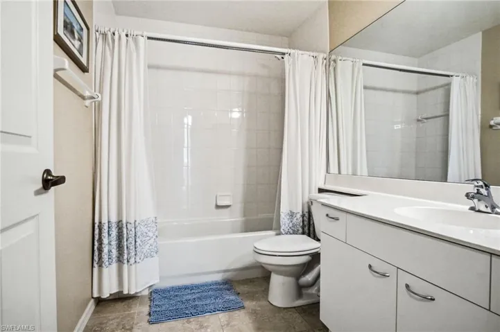 Bright and functional bathroom featuring a ceramic toilet, white vanity with dual sinks and chrome hardware, and a bathtub/shower combination with white subway tile surround and coordinating shower curtain