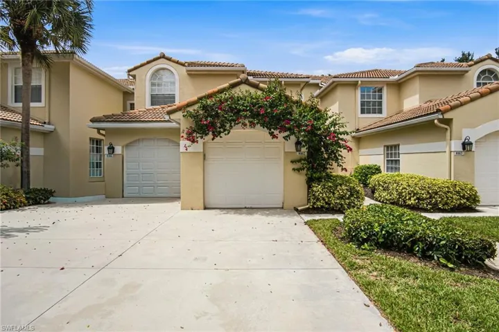 Elegant Mediterranean-inspired residence featuring a pristine concrete driveway, two-car garage with panel doors, and cream stucco exterior with clay tile roofing