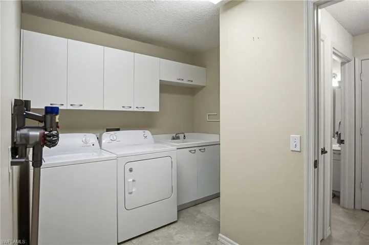 Dedicated laundry room featuring side-by-side white appliances, ample cabinetry with overhead storage, stainless steel sink with faucet, concrete flooring, and direct access to additional living spaces
