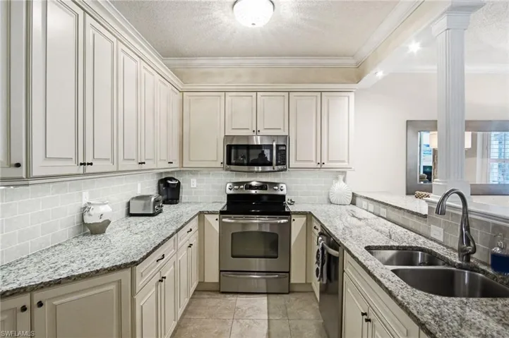 U-shaped kitchen featuring white cabinetry, light-colored countertops, a subway tile backsplash, stainless steel appliances, and tile flooring