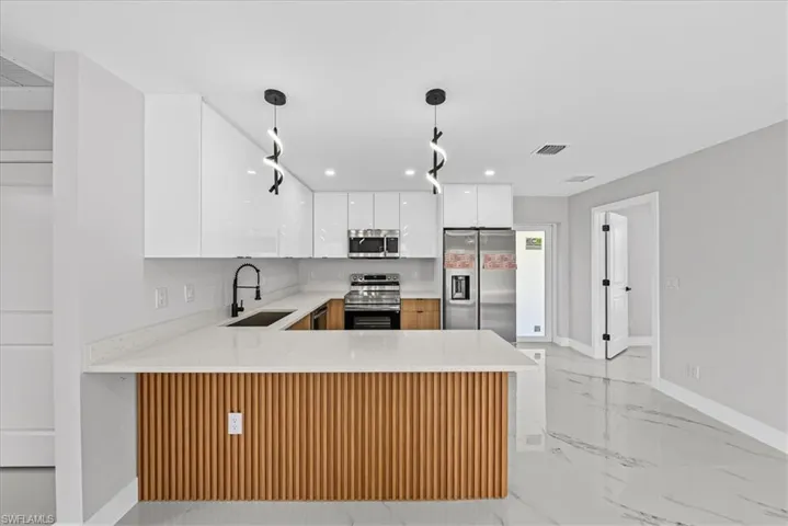 Kitchen featuring a breakfast bar with wood paneling, white shaker-style cabinetry, stainless steel appliances, and a matte black faucet