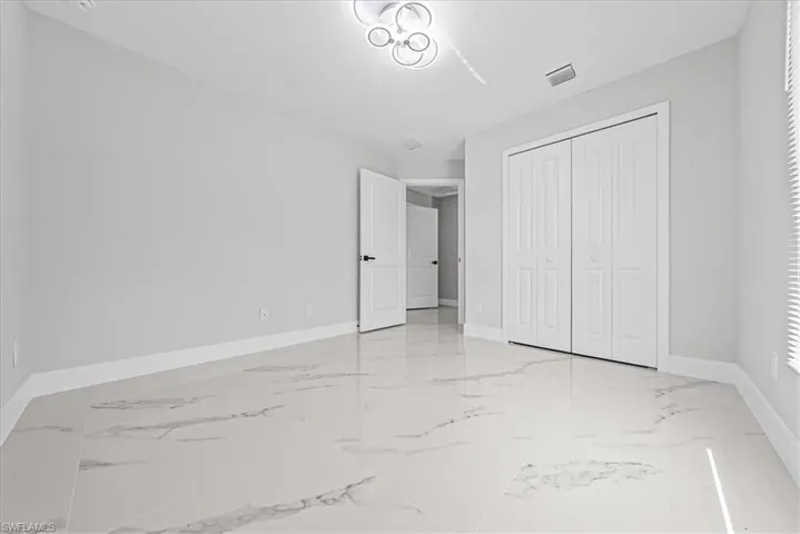 Spacious room featuring large format tile flooring, modern ceiling light fixture, bi-fold closet doors, and recessed lighting