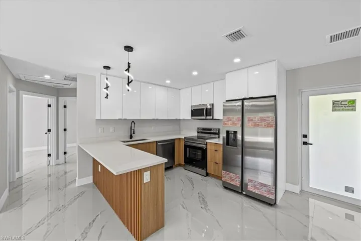 Kitchen featuring white high-gloss upper cabinetry, wood-finish lower cabinetry, a white countertop peninsula, and stainless steel appliances