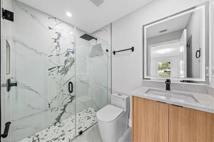 Glass-enclosed shower with large format marble-look tile and mosaic flooring