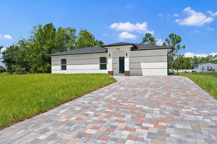 Modern residence featuring a striking geometric facade with clean lines and neutral exterior finishes, complemented by an expansive permeable paver driveway in a mixed-tone brick pattern
