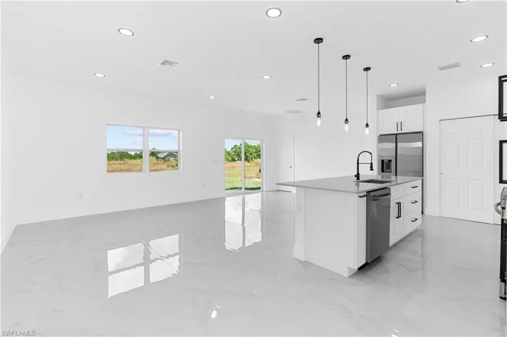 Kitchen with recessed lighting, open floor plan, an island with sink, pendant lighting, and light marble finish flooring
