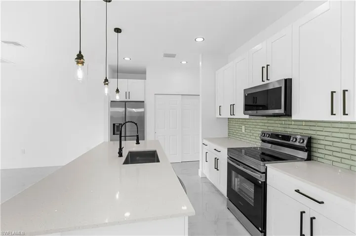 Kitchen with appliances with stainless steel finishes, light marble finish floors, pendant lighting, a kitchen island with sink, and light stone countertops