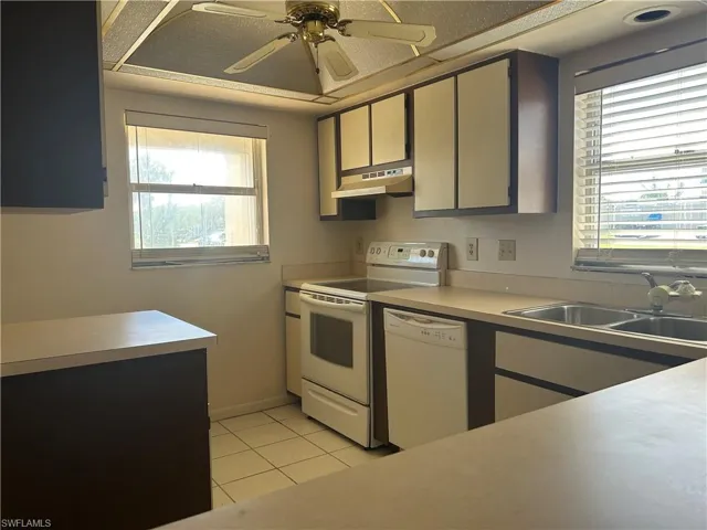 Kitchen featuring white appliances, light tile patterned floors, a ceiling fan, under cabinet range hood, and light countertops
