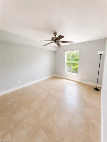 Spacious room featuring neutral wall tones, large format tile flooring, a window providing natural light, and a ceiling fan with integrated lighting