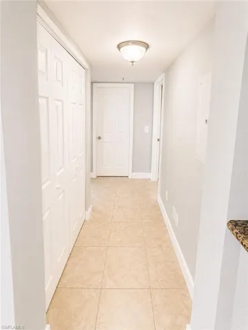 Hallway featuring neutral wall paint, tiled flooring, white baseboards, and a semi-flush mount ceiling light