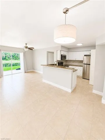 Open-concept living area with large format tile flooring, a kitchen island with stone countertops, white shaker cabinetry, stainless steel appliances, and a sliding glass door opening to outdoor space