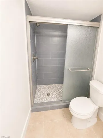 Tiled shower with frosted sliding glass doors, pebble flooring, and brushed nickel fixtures