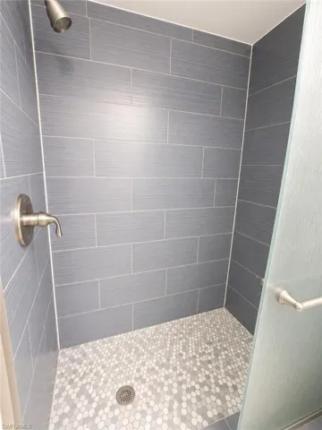 Walk-in shower featuring elongated rectangular wall tiles, hexagonal mosaic floor tiles, a brushed nickel showerhead, and a frosted glass shower door with a brushed nickel handle