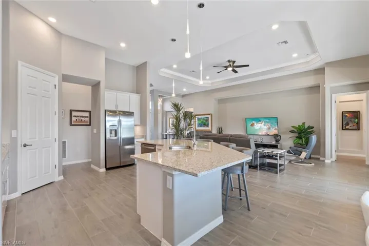 Kitchen featuring ceiling fan, a sink, a raised ceiling, stainless steel appliances, and an island with sink