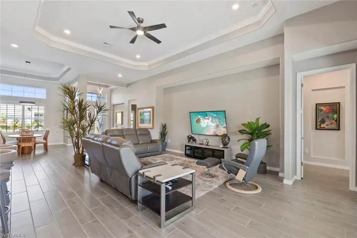 Living room featuring baseboards, ceiling fan, recessed lighting, a raised ceiling, and light wood finished floors