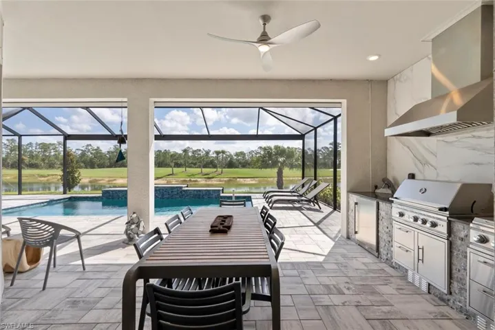 View of patio / terrace with a lanai, a ceiling fan, an outdoor pool, an outdoor kitchen, and a grill