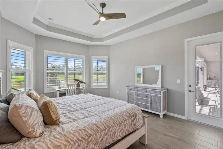 Bedroom featuring access to outside, light wood finished floors, a tray ceiling, and multiple windows