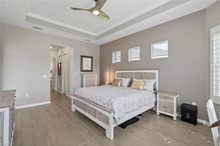 Bedroom featuring visible vents, crown molding, baseboards, wood tiled floor, and a tray ceiling