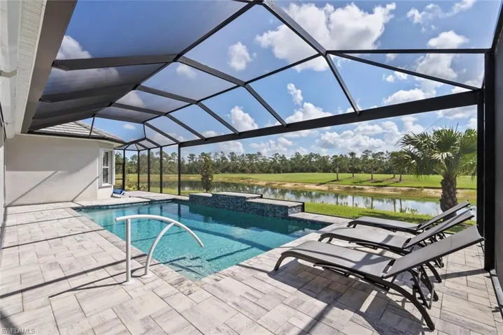 Pool featuring glass enclosure, a water view, and a patio