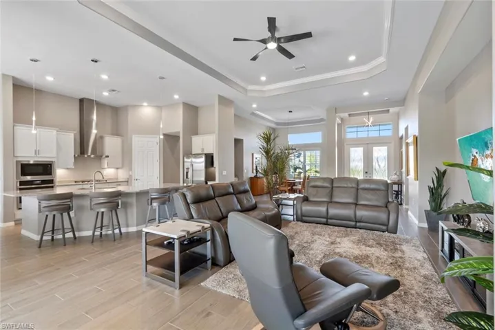 Living room with crown molding, recessed lighting, a tray ceiling, a ceiling fan, and light wood-style flooring