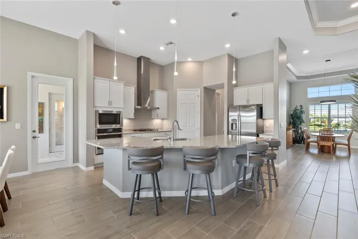 Kitchen with a spacious island, wall chimney range hood, a sink, light wood finished floors, and appliances with stainless steel finishes