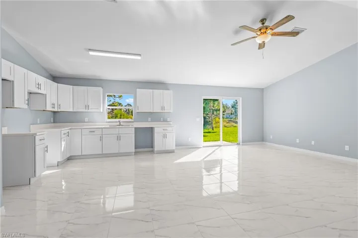 Kitchen with lofted ceiling, light countertops, light marble finish floors, white cabinets, and a ceiling fan