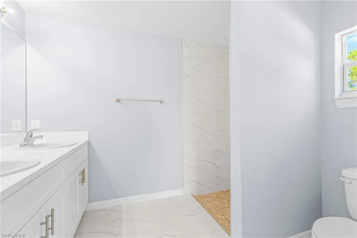 Full bathroom with light marble finish floors, double vanity, and a marble finish shower