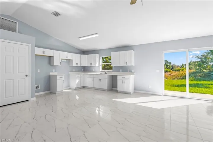 Kitchen with vaulted ceiling, light marble finish floors, white cabinetry, light countertops, and ceiling fan