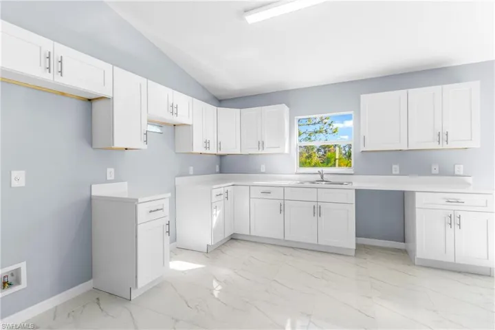 Kitchen with lofted ceiling, white cabinets, light countertops, and light marble finish flooring