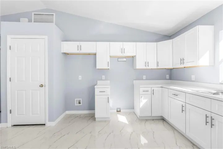 Kitchen featuring vaulted ceiling, white cabinetry, light countertops, and light marble finish flooring