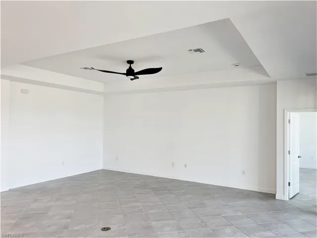 Unfurnished room with a raised ceiling, ceiling fan, and light tile patterned floors