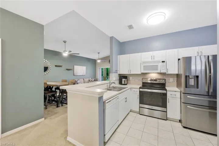Kitchen featuring kitchen peninsula, tasteful backsplash, ceiling fan, light carpet, and appliances with stainless steel finishes