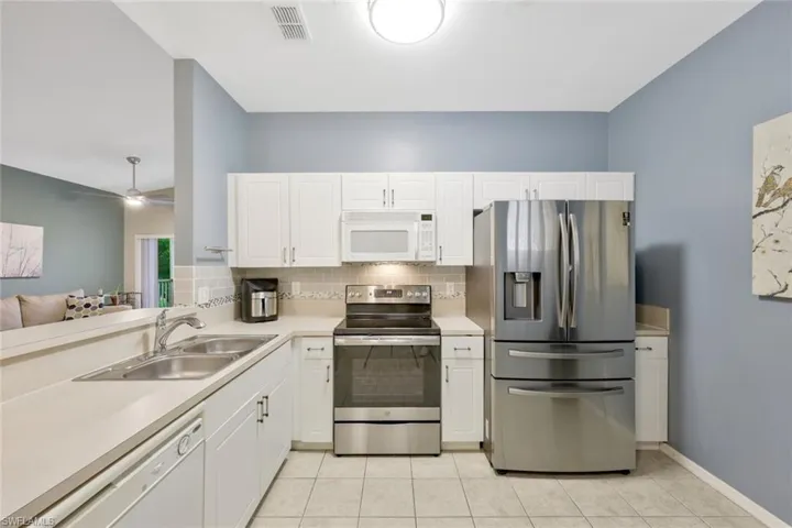 Kitchen featuring white cabinets, light tile flooring, stainless steel appliances, ceiling fan, and sink