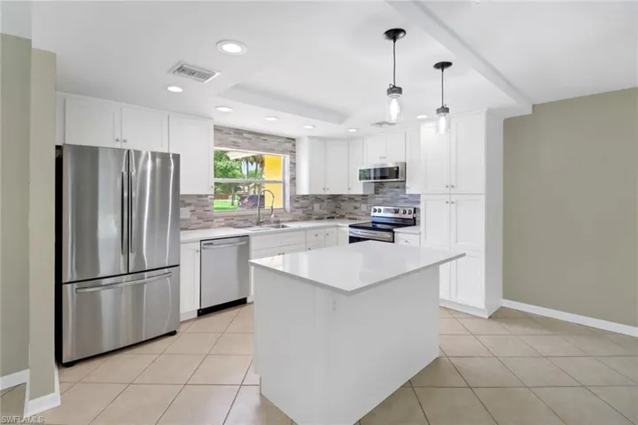 Kitchen with white cabinetry, hanging light fixtures, a tray ceiling, a kitchen island, and appliances with stainless steel finishes