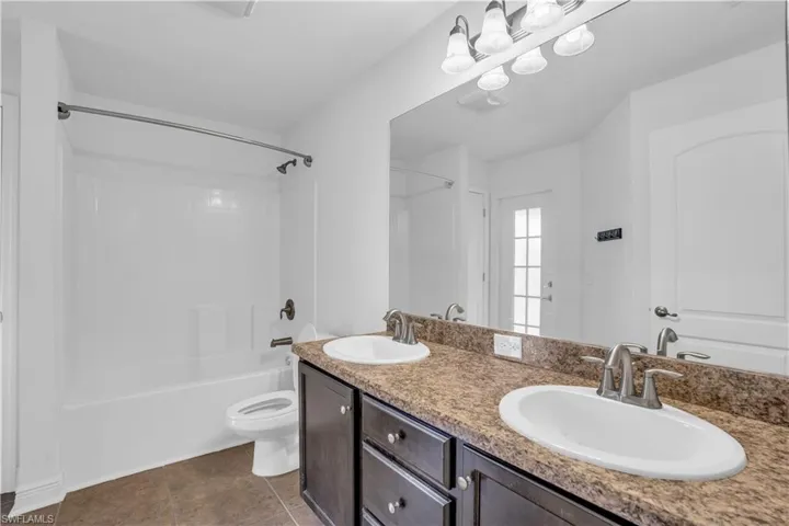 Full bathroom with tile patterned floors, dual bowl vanity,  shower combination, and toilet