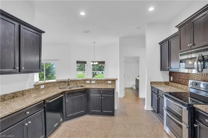 Kitchen featuring light tile patterned flooring, sink, light stone countertops, and stainless steel appliances