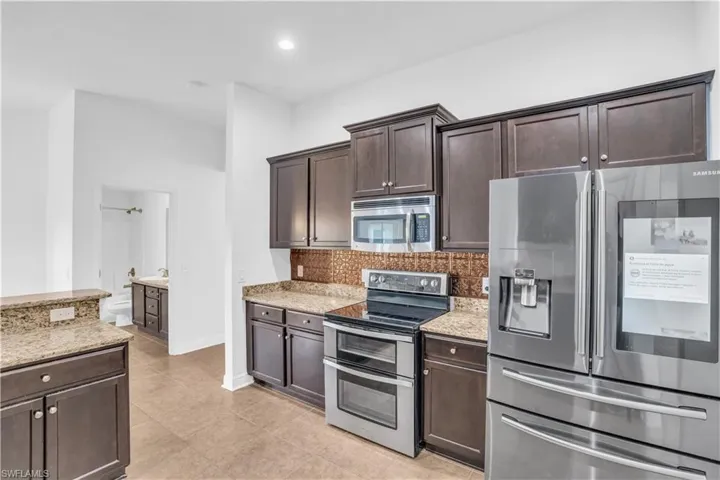 Kitchen featuring appliances with stainless steel finishes, light tile patterned flooring, light stone counters, and backsplash