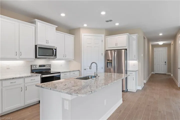 Kitchen with stainless steel appliances, sink, decorative backsplash, light wood-type flooring, and an island with sink