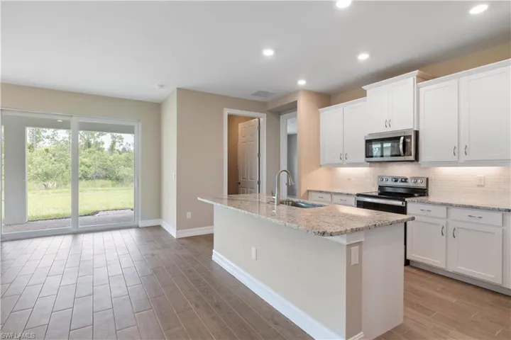 Kitchen featuring white cabinets, light stone counters, appliances with stainless steel finishes, backsplash, and a kitchen island with sink